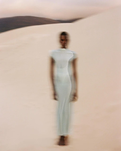 Motion-blurred full shot of an African woman in a long dress walking across sand dunes against the background of a mountain ridge.