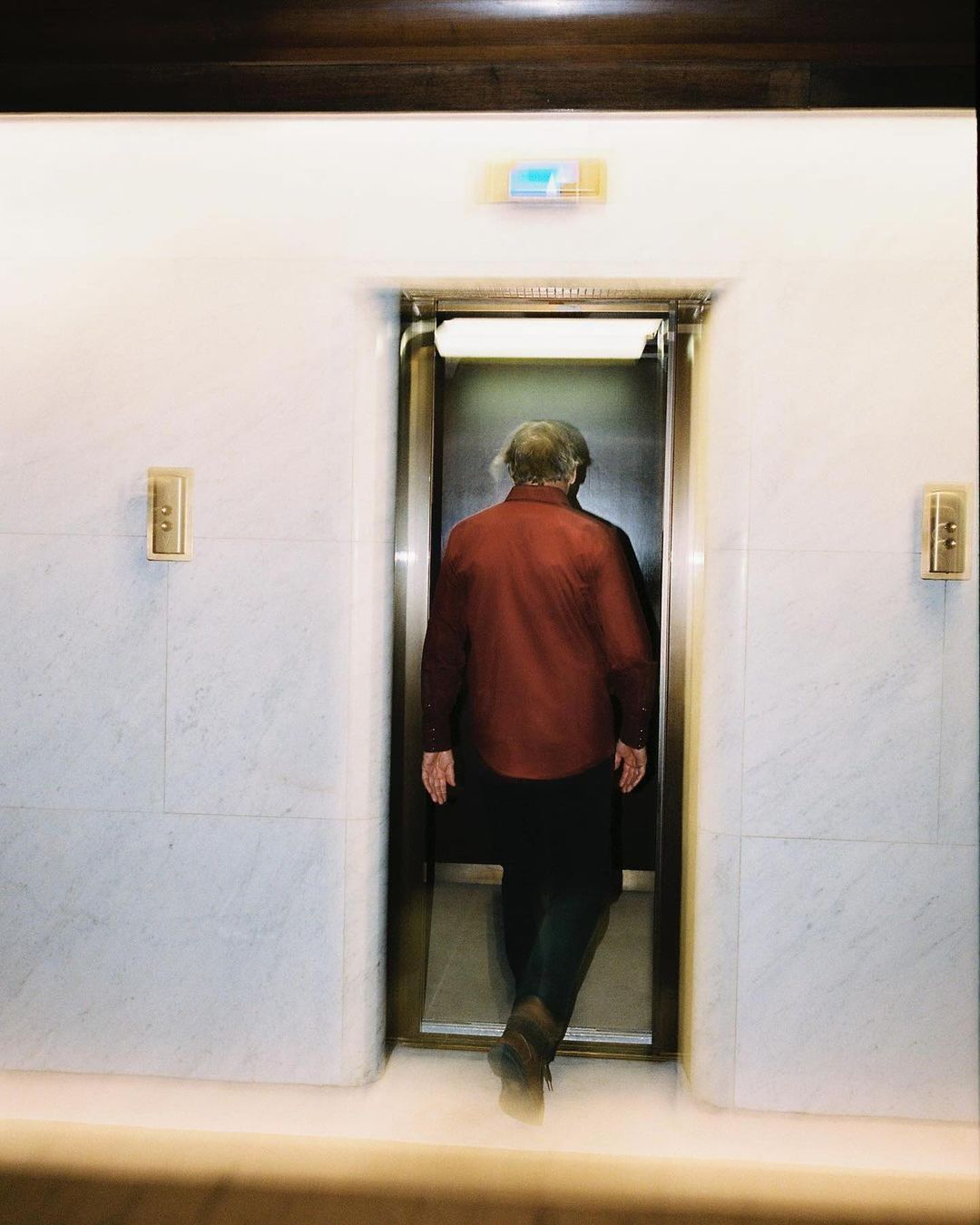 An elderly person walks through an elevator, captured with blurred motion to convey movement in an indoor environment.