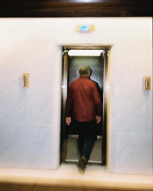 An elderly person walks through an elevator, captured with blurred motion to convey movement in an indoor environment.