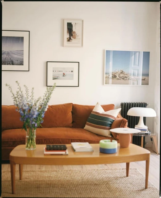 Living room interior featuring a brown corduroy sofa, a wooden coffee table with books and a vase of blue flowers, and framed art on the wall.