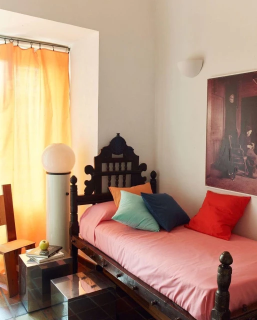 Bedroom interior with a wooden bed, colorful pillows, a floor lamp, and a window with orange curtains. Interior design, furniture.