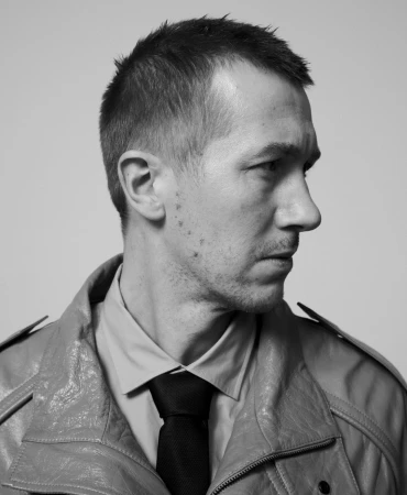 Monochrome portrait of a man in a collared shirt, tie, and jacket looking to the side against a neutral background.