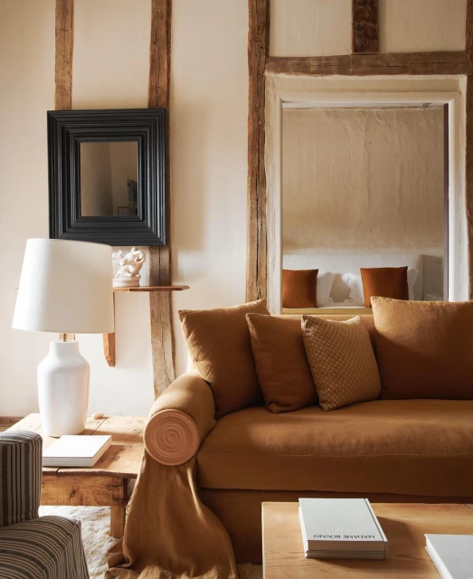 Cozy living room interior with an ochre couch, decorative pillows, neutral walls, and wooden architectural details for a warm aesthetic.