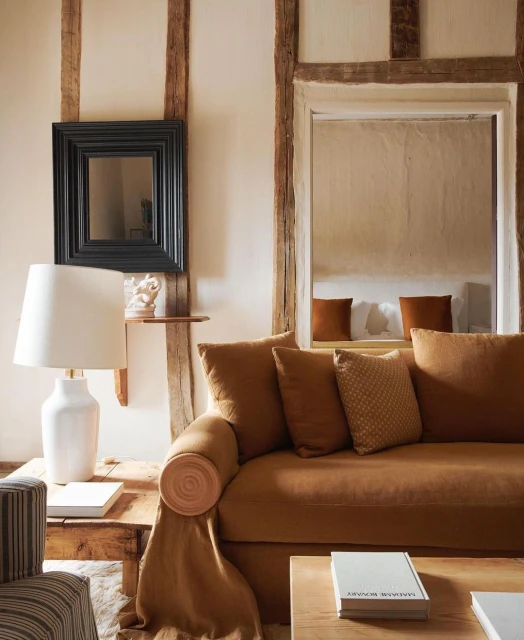 Living room interior featuring a caramel brown sofa with throw pillows and a blanket, a white lamp, and rustic wood trim details.