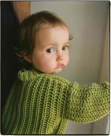 Young child wearing a green knitted sweater looking over their shoulder in Madrid by photographer Pablo Zamora.