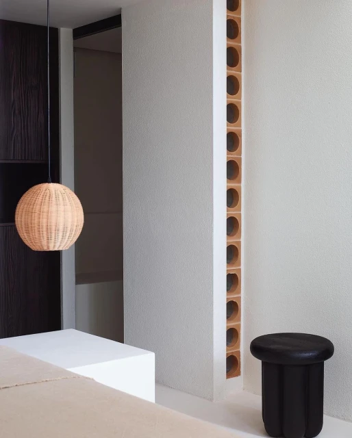Interior space with a rattan pendant light, black side table, and architectural details in neutral tones, creating a minimalist aesthetic.