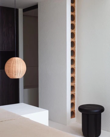 Interior space with a rattan pendant light, black side table, and architectural details in neutral tones, creating a minimalist aesthetic.