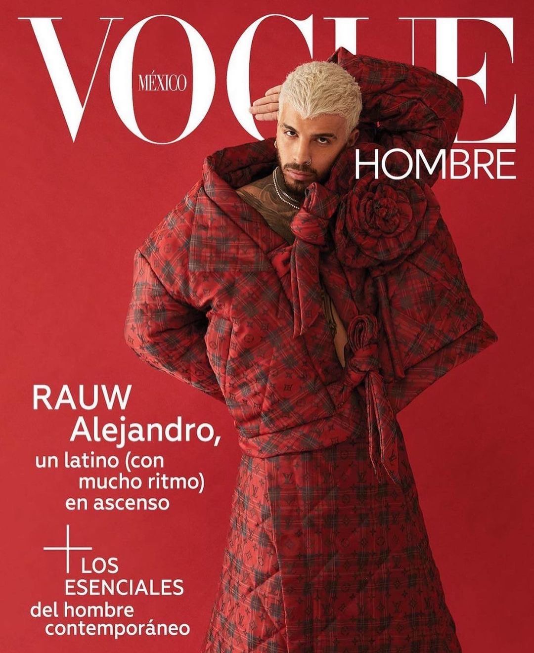 Man with platinum hair poses on a Vogue Mexico Hombre cover wearing a red plaid robe-like jacket. Red background with white Vogue text.