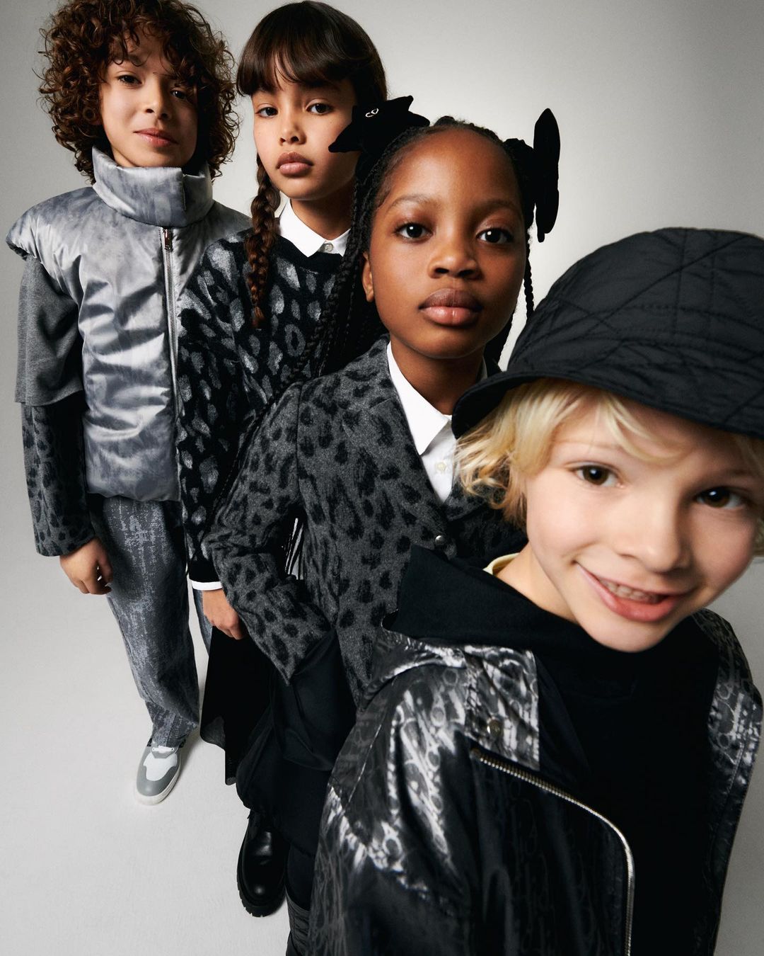 Four stylish children in a row, wearing patterned jackets and hats in a studio setting. Fashion advertisement with children models.