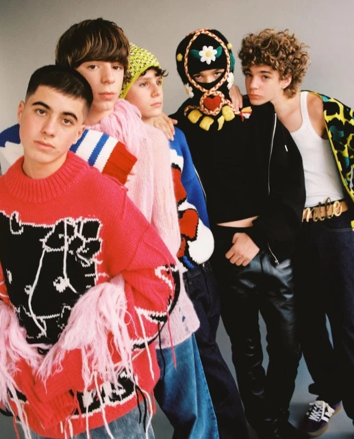 Group portrait of five teenage males in casual fashion with colorful sweaters and jeans posing against a gray studio backdrop.