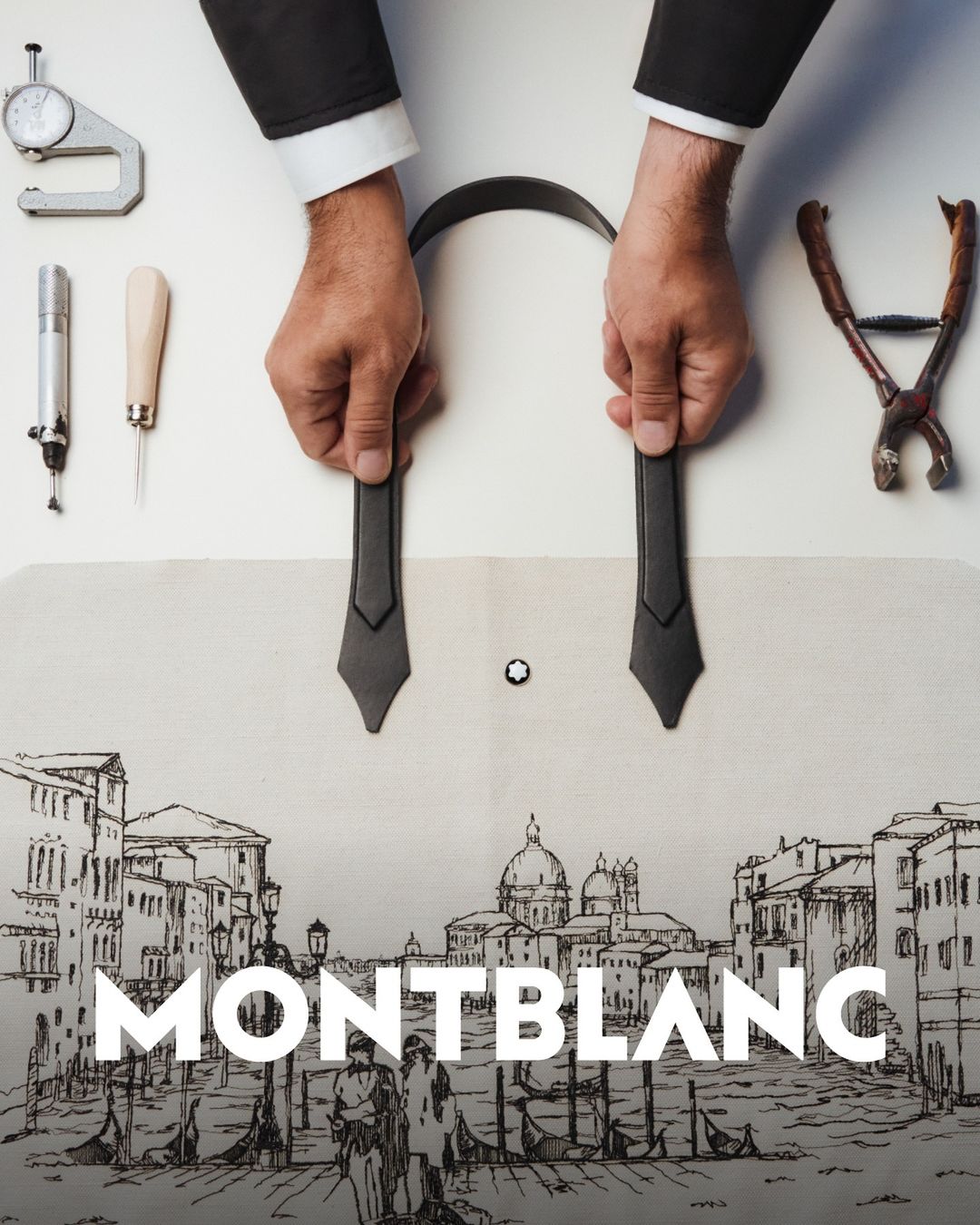 Overhead studio shot of hands crafting a black leather belt with precision tools against a backdrop featuring a sketch of Venice.