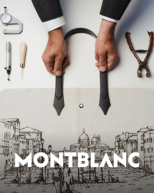Overhead studio shot of hands crafting a black leather belt with precision tools against a backdrop featuring a sketch of Venice.