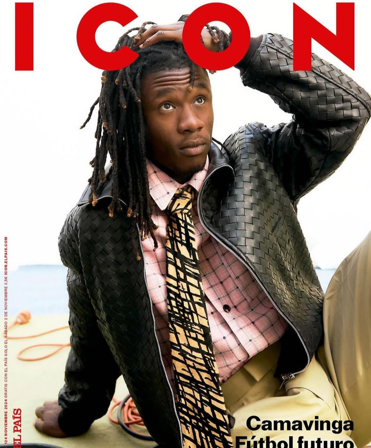 Magazine cover featuring an adult male with dreadlocks, wearing a pink patterned shirt, tie, and black jacket; holding his hand to his hair.