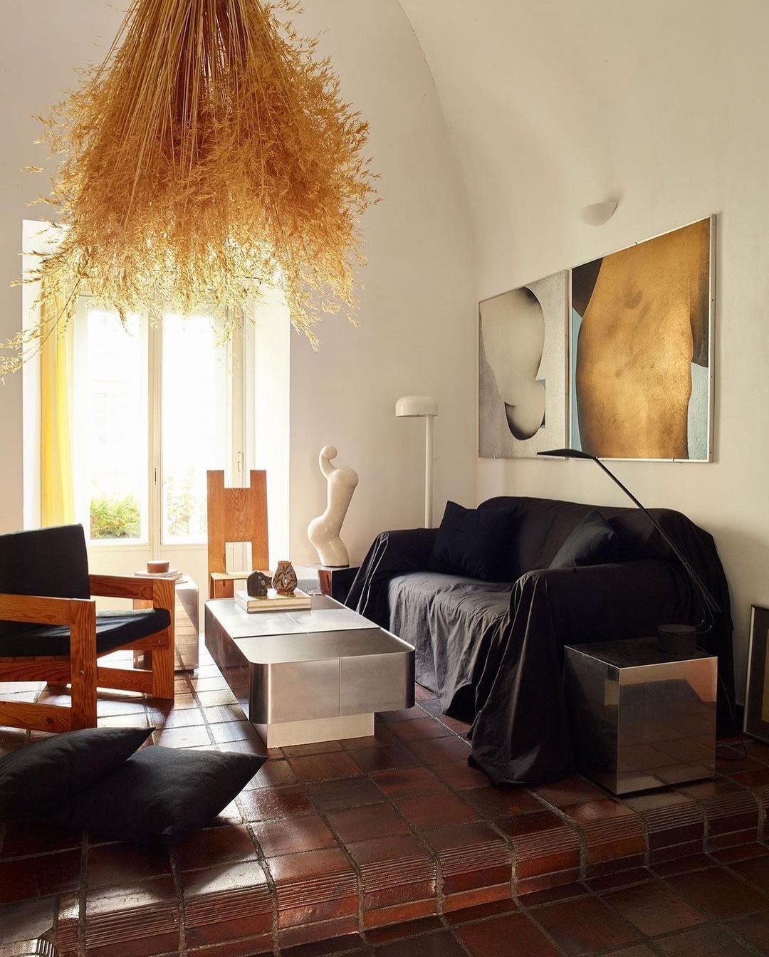 Interior view of a living room featuring neutral color palette, tiled floor, dark sofa, and a dried floral arrangement.