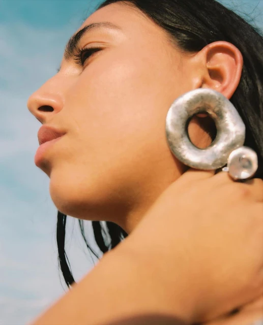 Portrait of a woman with silver earrings, captured with a low angle against a bright sky, showcasing minimalist beauty and style.