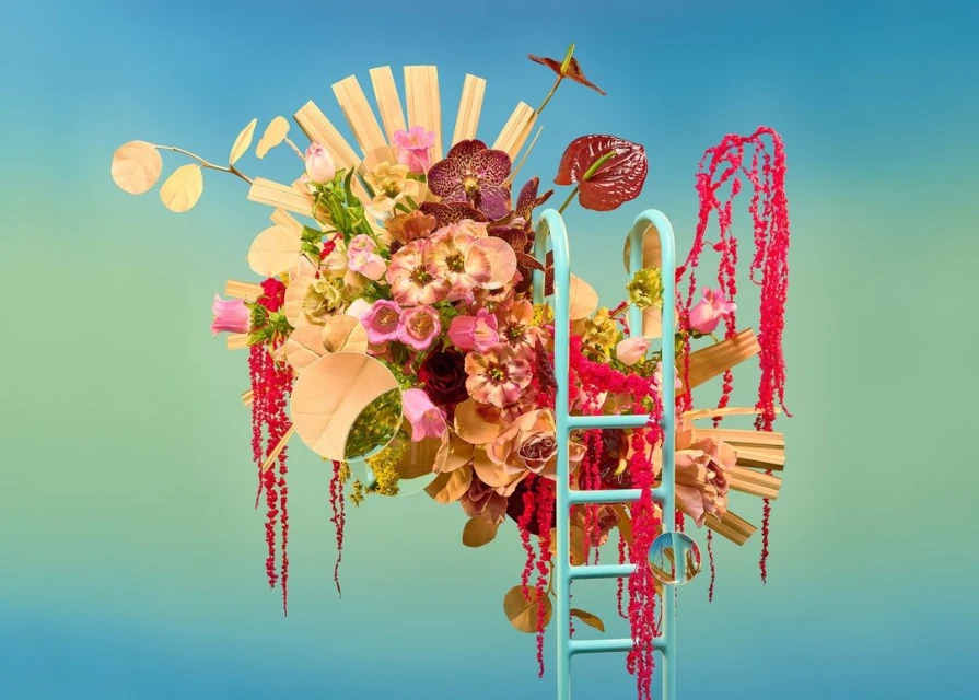 Floral arrangement with orchids, roses, and amaranthus on a light blue and green gradient background, next to a light blue step ladder.