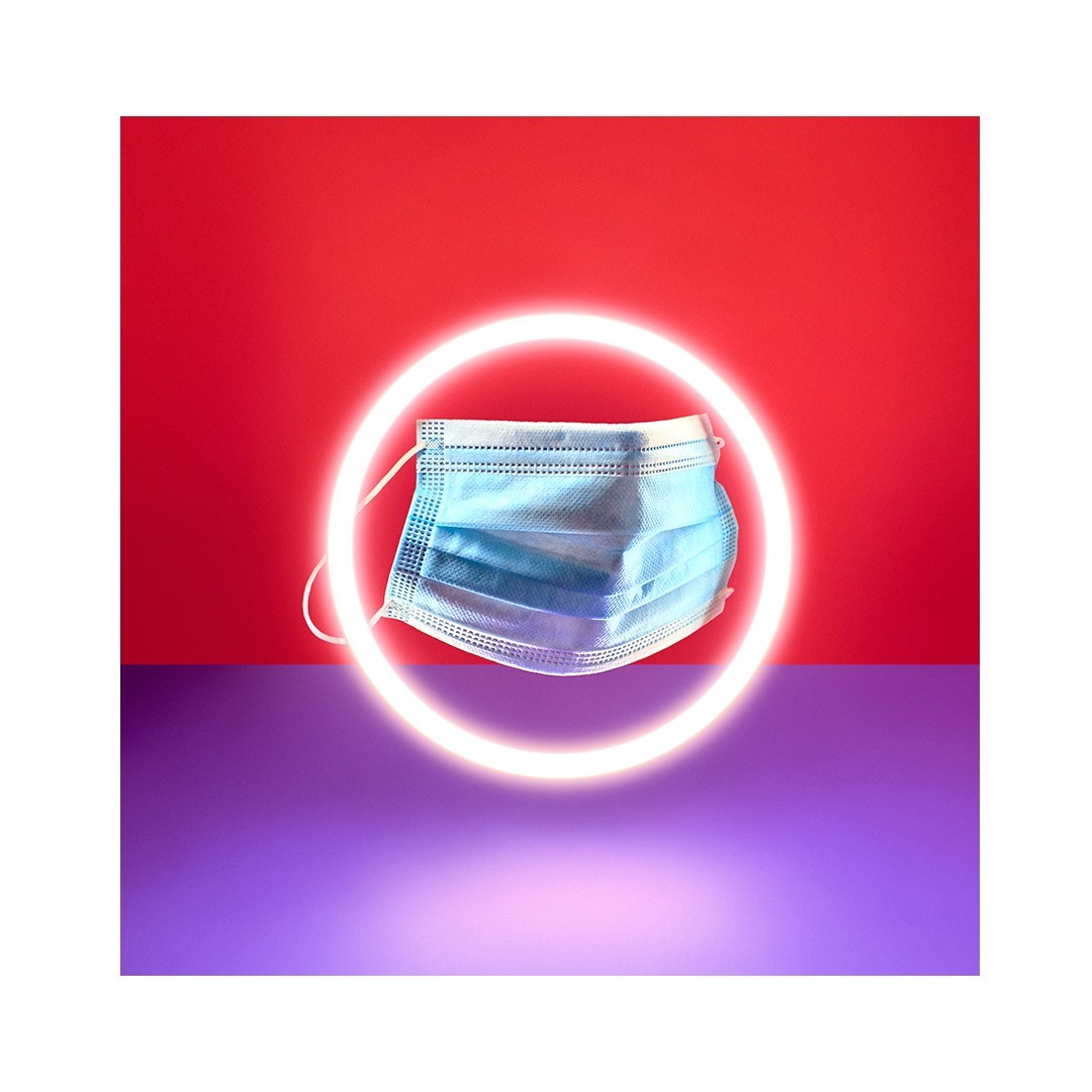 Medical face mask on a red and purple background with a neon ring light highlighting the object in a visually striking composition.