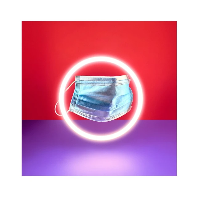 Medical face mask on a red and purple background with a neon ring light highlighting the object in a visually striking composition.