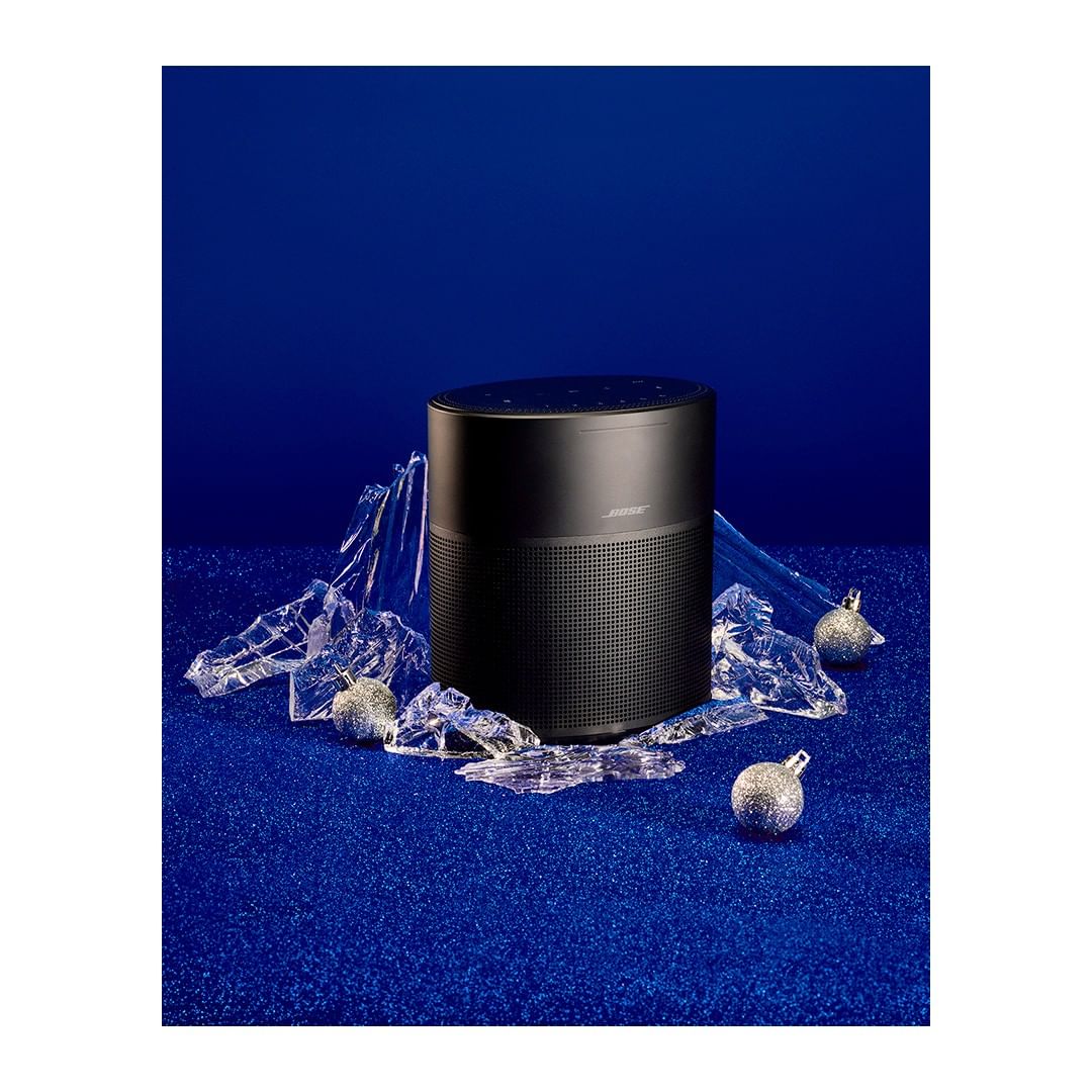 Bose speaker showcased on a blue glittery surface with clear plastic pieces and spherical silver ornaments, creating a striking product display.