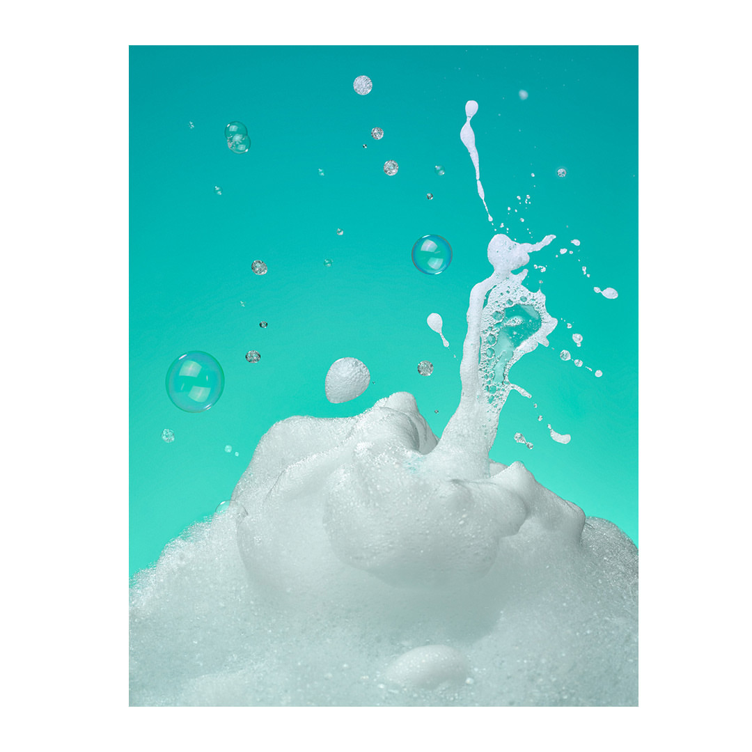 Bubbles and foam splash against a bright cyan background. Concept photography featuring a clean, fresh aesthetic for product promotion.