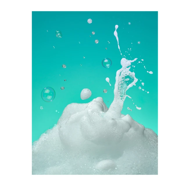 Bubbles and foam splash against a bright cyan background. Concept photography featuring a clean, fresh aesthetic for product promotion.