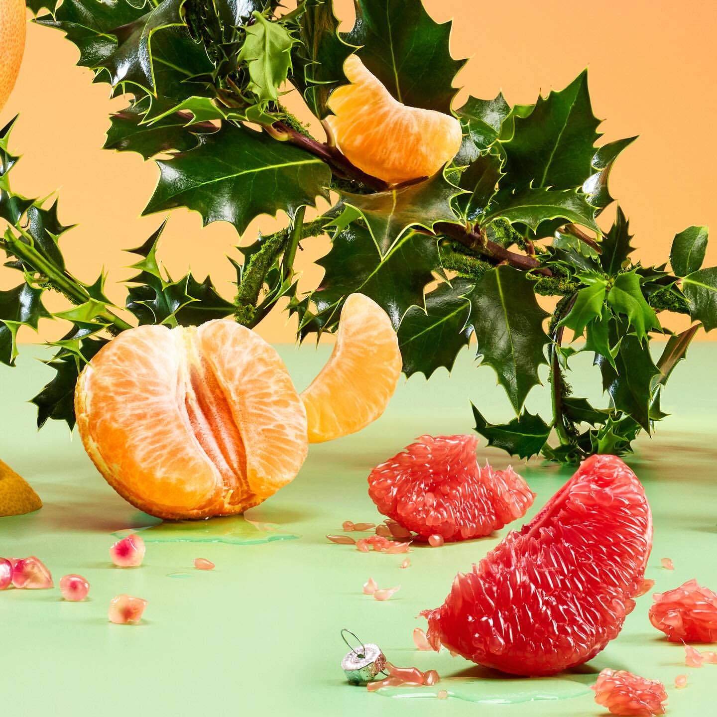 Festive food still life of citrus fruits including tangerines and grapefruit with holly and a Christmas ornament on a green table.