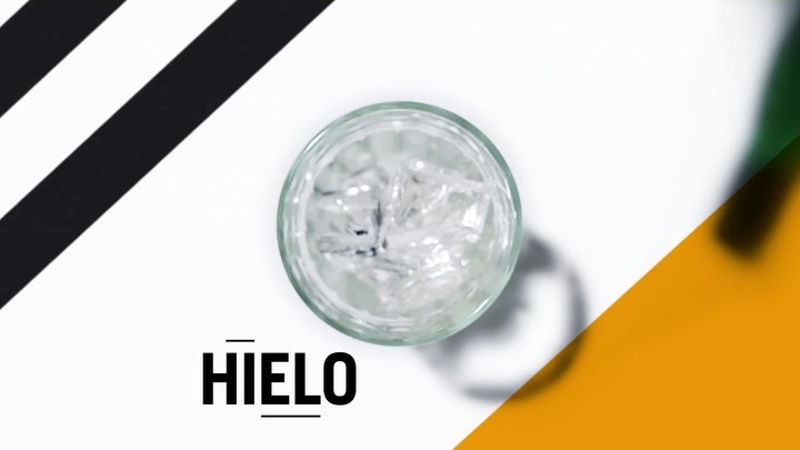 Overhead shot of a clear glass filled with ice cubes, set against a dynamic white background with black, gold, and green accents.