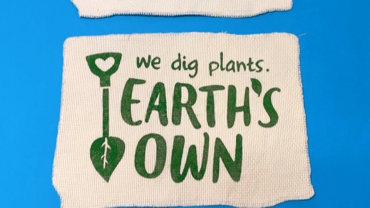 Graphic design on fabric patches features green text 'We Dig Plants, Earth's Own' and a shovel with a heart-shaped head against a blue backdrop.