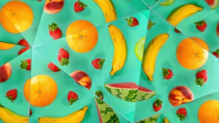 Overhead flat lay of various fruits including oranges, bananas, strawberries, watermelon, peach, and green apple on a blue background.