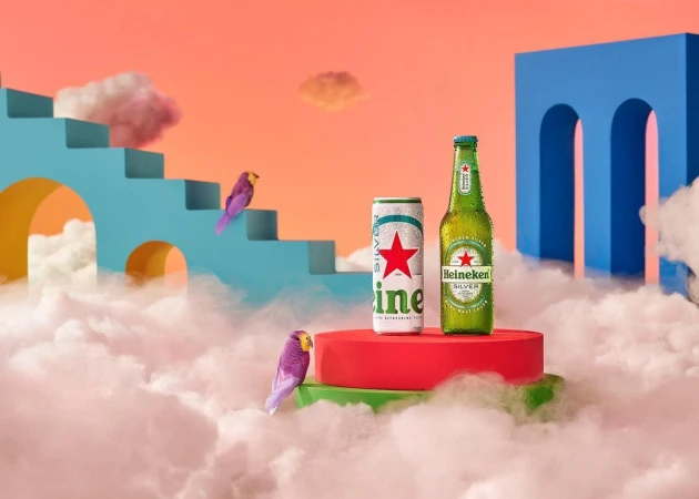 Heineken Silver products displayed on a red platform, surrounded by white clouds, birds, and a blue architectural structure.