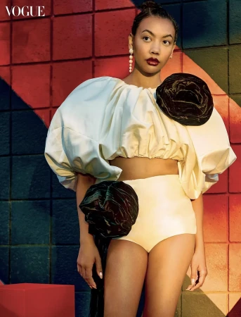 Fashion model in a voluminous cream puff-sleeve crop top with black rosette accents posing before a geometric colored grid wall.