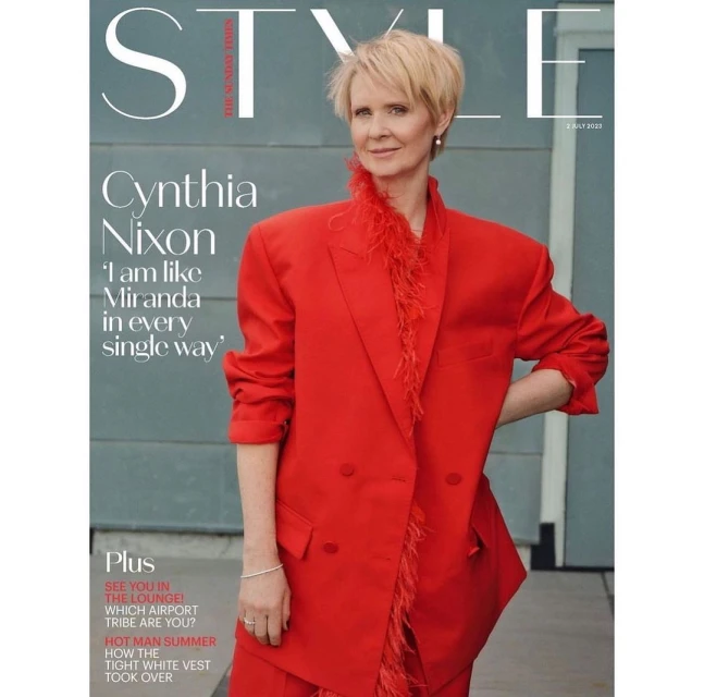 Cynthia Nixon on the cover of Style magazine wearing a red suit with feather trim, posing in front of a grey wall with a doorway.