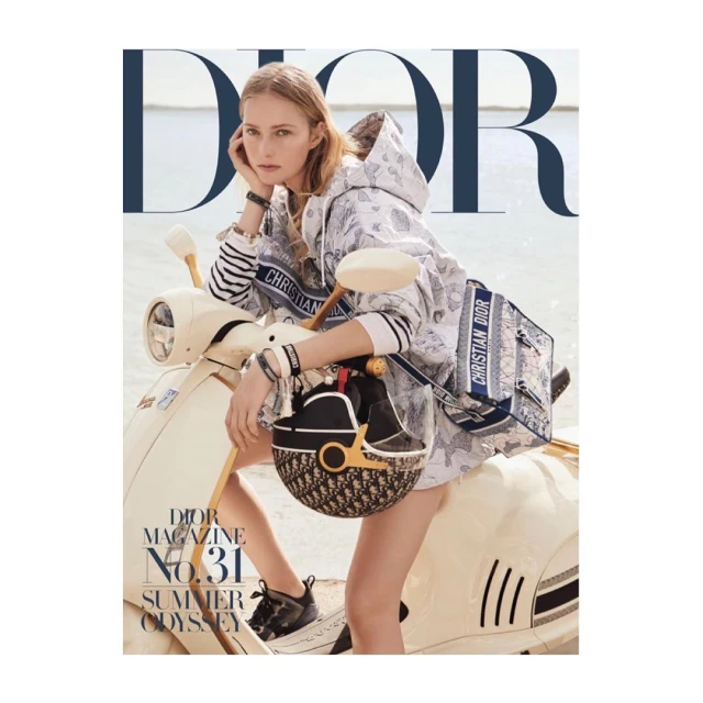 Blonde fashion model poses with a cream-colored Vespa scooter next to Dior handbag and helmet on a fashion magazine cover.