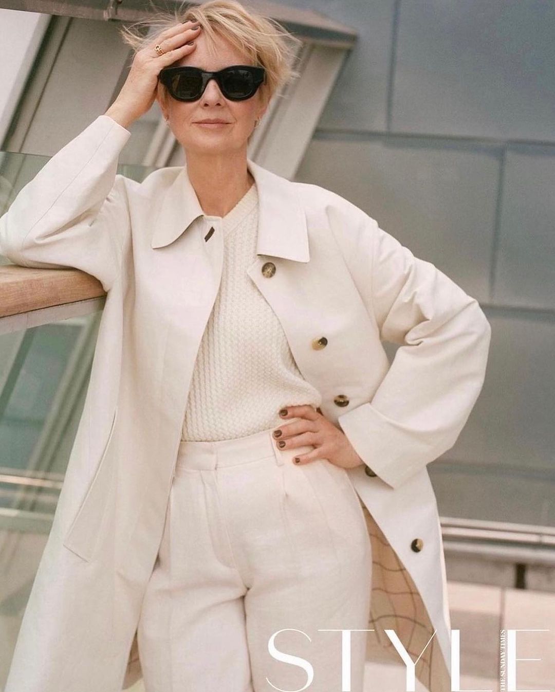 Mature woman in sunglasses wearing a white coat and trousers posing outdoors in London