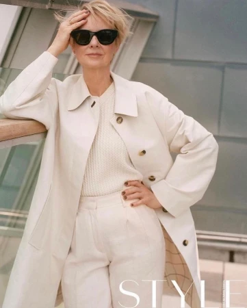Mature woman in sunglasses wearing a white coat and trousers posing outdoors in London