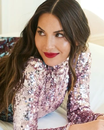 Olivia Munn wearing a sparkly sequin dress with red lipstick looking over her shoulder