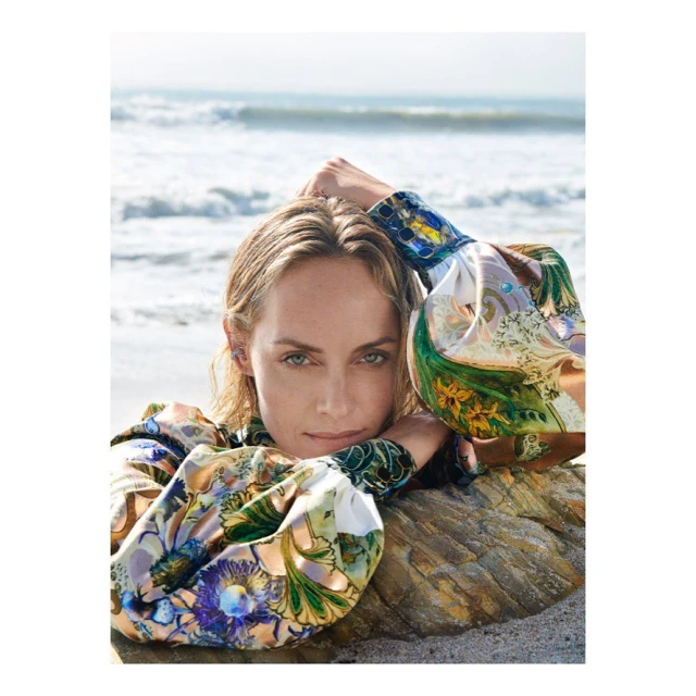 Woman with patterned top rests on a rock at the beach. Ocean waves and light sand create a peaceful backdrop for this portrait.