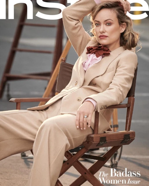 Olivia Wilde in a tan suit sits in a director's chair for InStyle magazine, set against an outdoor urban backdrop, fashion-editorial.