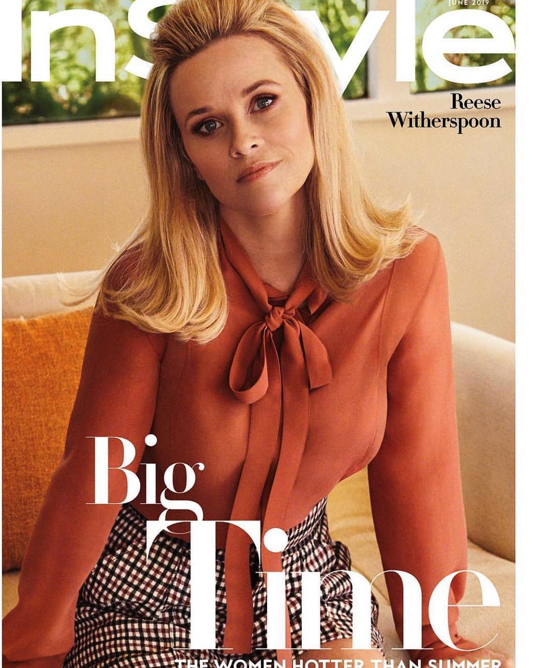 Reese Witherspoon poses on the cover of InStyle magazine, wearing a bow blouse and checkered skirt indoors with a neutral backdrop.