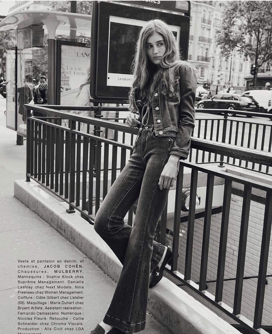 Outdoor fashion portrait in Paris of a young woman wearing a denim jacket and bell-bottom jeans leaning against a metal railing.