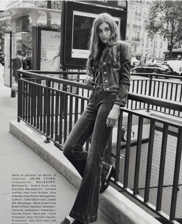 Outdoor fashion portrait in Paris of a young woman wearing a denim jacket and bell-bottom jeans leaning against a metal railing.