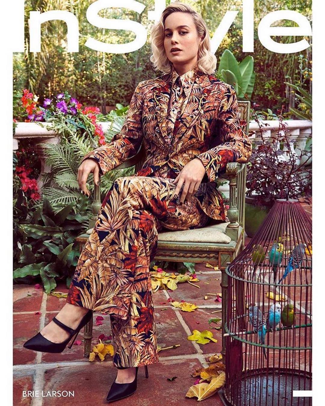 Brie Larson is sitting on a chair outside, wearing a brown botanical-print pantsuit on the cover of InStyle magazine.