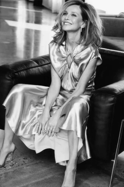 Black and white portrait of a middle-aged woman with shoulder-length hair sitting on a black chair wearing a satin dress and heels.