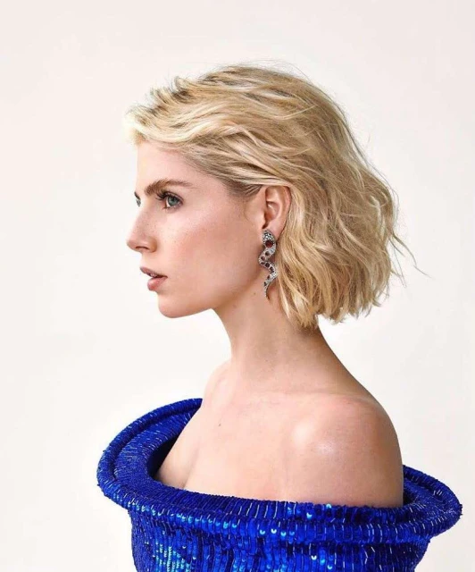 Blonde woman in off-shoulder blue dress poses in a studio portrait with snake earrings. Beauty and fashion editorial style.