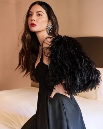 Elegant woman in a black dress with a feather accessory posing indoors. The image features a formal portrait against a neutral backdrop.