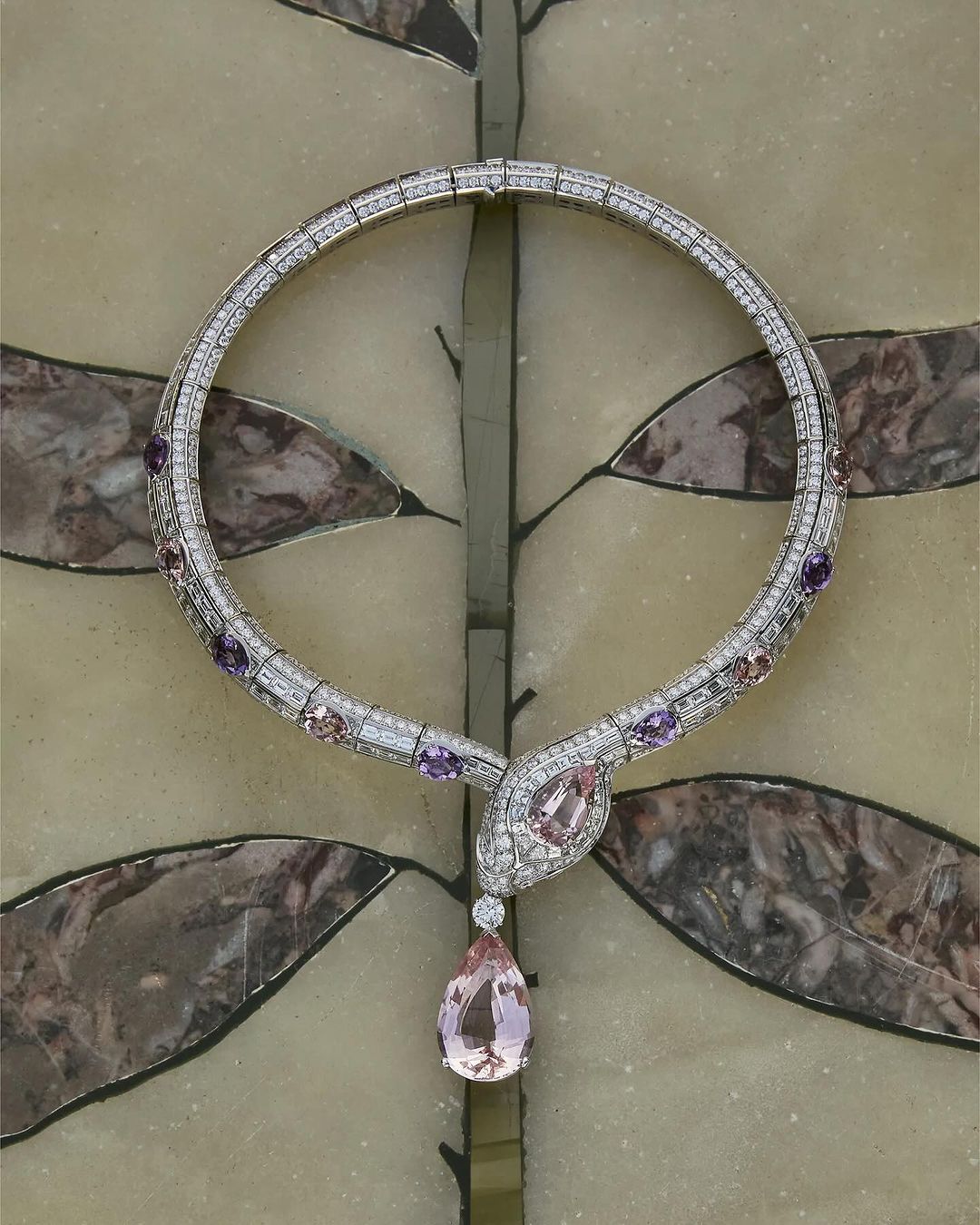Elegant snake-shaped necklace featuring diamonds, amethysts, and morganite gemstone pendant on a decorative surface with neutral hues.