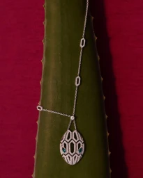 Diamond necklace draped over a textured green plant stem against a deep red background