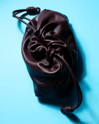 Dark brown leather drawstring pouch handbag resting on a bright blue surface under studio lighting.
