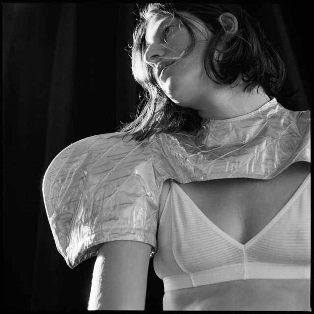 Black and white portrait of a woman in a bra and unique shoulder piece against a dark background. Side view. Minimalist fashion.