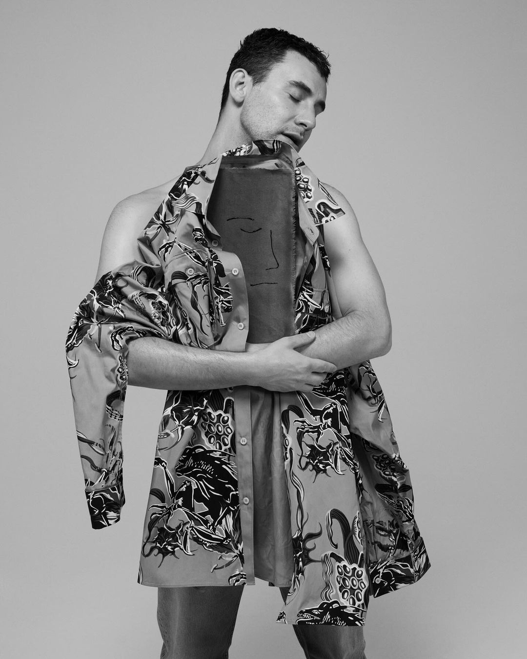 Monochrome portrait of a man holding a patterned shirt up to his face in a studio by Paola Kudacki.